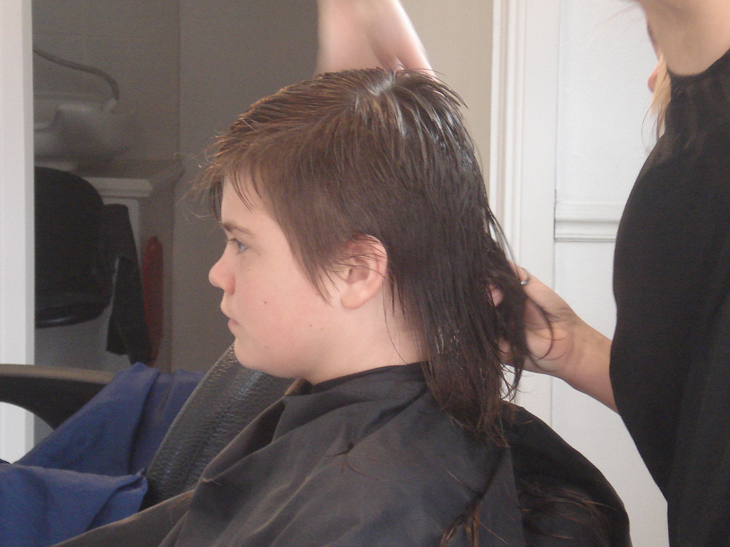 Auf dem Bild ist ein Kind zu sehen. Die Haare werden vorne kurz und hinten lang geschnitten.