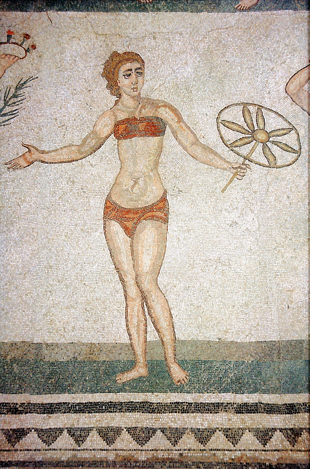 Auf dem Bild ist ein Mosaik. Auf dem Mosaik ist eine Frau im Bikini. Die Frau macht Sport.