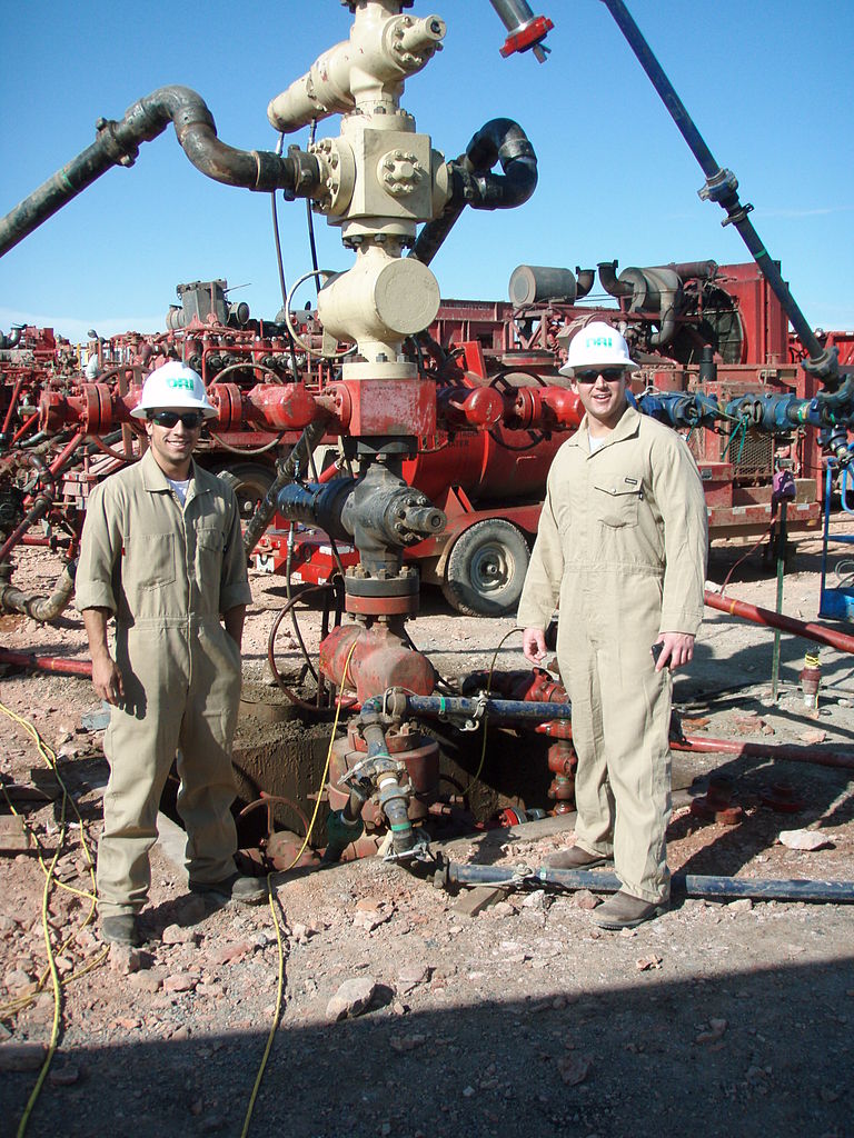 Auf dem Bild ist eine Fracking-anlage und zwei Arbeiter zu sehen