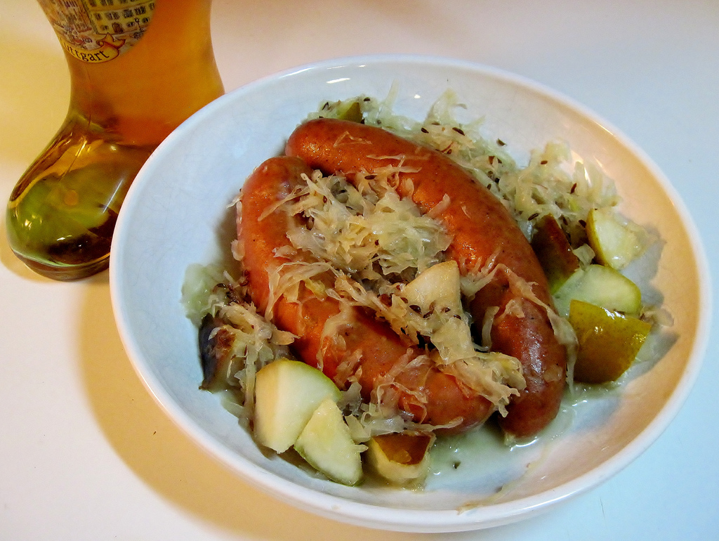 Auf dem Bild ist ein Teller mit Sauerkraut, Bratwurst und Kartoffeln zu sehen